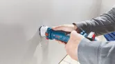 コードレス乾式壁ルーターを使用して乾式壁に長方形の穴を開ける人。