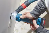 集塵機能付きの電動工具を使用して、乾式壁に長方形の穴を開ける人。
