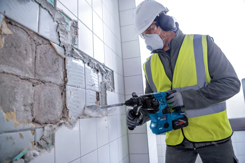 安全装置を装着した人が回転ハンマーを使用して壁からタイルを取り外します。.