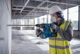 安全装備を身に着けた人が回転ハンマーでコンクリートの壁に穴を開けています。