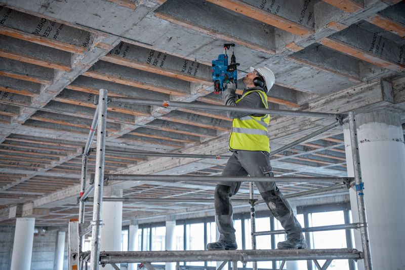 安全装備を身に着けた人が建設現場でコンクリートの天井に穴を開けています。.