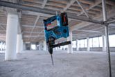 未完成の建設現場の金属パイプにぶら下がっているコードレス回転ハンマー。
