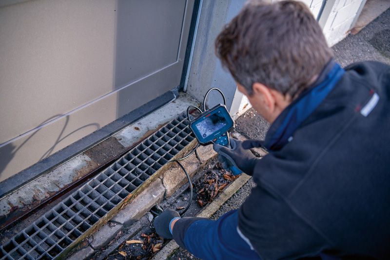 安全装備を装着した人が検査カメラで排水溝を検査しています。.