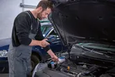 作業服を着た人が検査カメラを使って車のエンジンルームを検査しています。