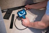 狭い床面空間内を検査するために検査カメラを操作する人。