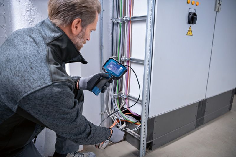 安全装備を装着した人が検査カメラを使用して電気配線を検査します。.