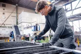 安全装置を装着した人が作業場で電動工具を使って金属の梁を固定しています。