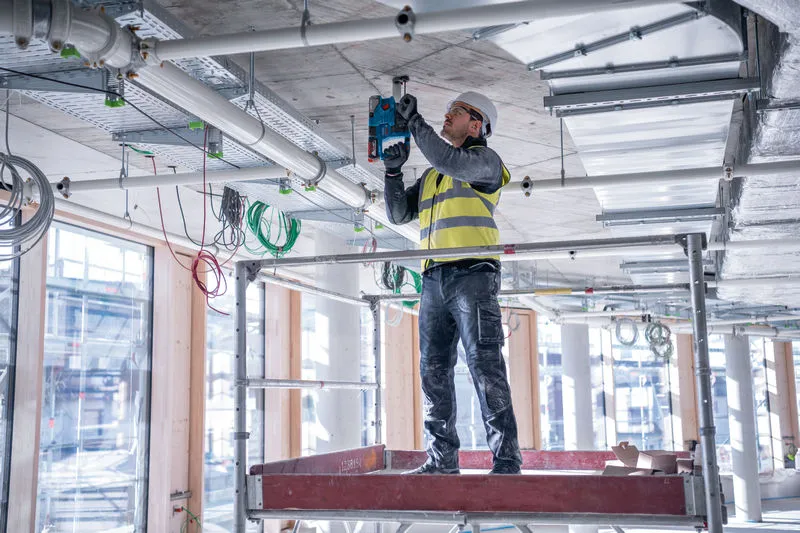 安全装備を身に着けた人が建設現場でコンクリートの天井に穴を開けています。.