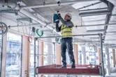 安全装備を身に着けた人が建設現場でコンクリートの天井に穴を開けています。.