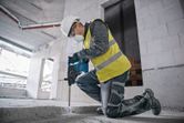 安全装備を身に着けた人が建設現場でハンマードリルを使用してコンクリートを破壊しています。