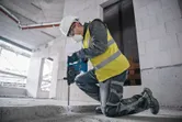 安全装備を身に着けた人が建設現場でハンマードリルを使用してコンクリートを破壊しています。