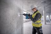 安全装備を身に着けた人が建設現場でコンクリートの壁に穴を開けています。