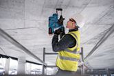 安全装置を装着した人が電動工具を使用してコンクリートの天井に穴を開けています。