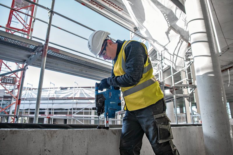 安全装備を身に着けた人が建設現場でコンクリートに穴を開けています。.