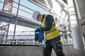 安全装備を身に着けた人が建設現場でコンクリートに穴を開けています。