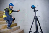安全装備を身に着けた人が三脚に取り付けたレーザーレベルツールを使用して壁に印を付けます。