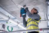 安全装備を身に着けた人が建設現場でコンクリートの天井に穴を開けています。.