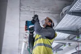 安全装備を身に着けた人が建設現場でコンクリートの天井に穴を開けています。.