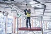 安全装備を身に着けた人が建設現場でコンクリートの天井に穴を開けています。.