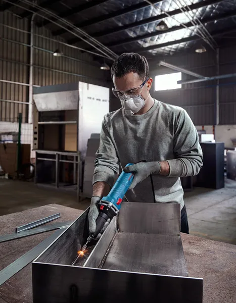 安全装備を身に着けた人が工場内で金属を研磨しています。.