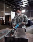 安全装備を身に着けた人が工場内で金属を研磨しています。.