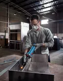 安全装備を身に着けた人が工場内で金属を研磨しています。.