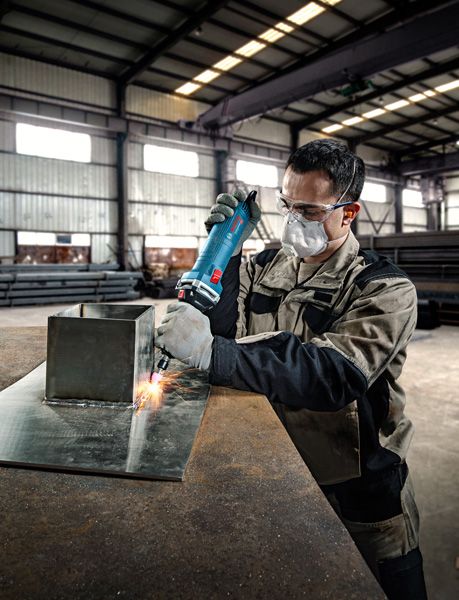 安全装備を身に着けた人が金属板にストレートグラインダーを使用しています。.