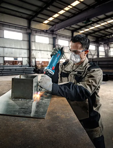 安全装備を身に着けた人が金属板にストレートグラインダーを使用しています。.