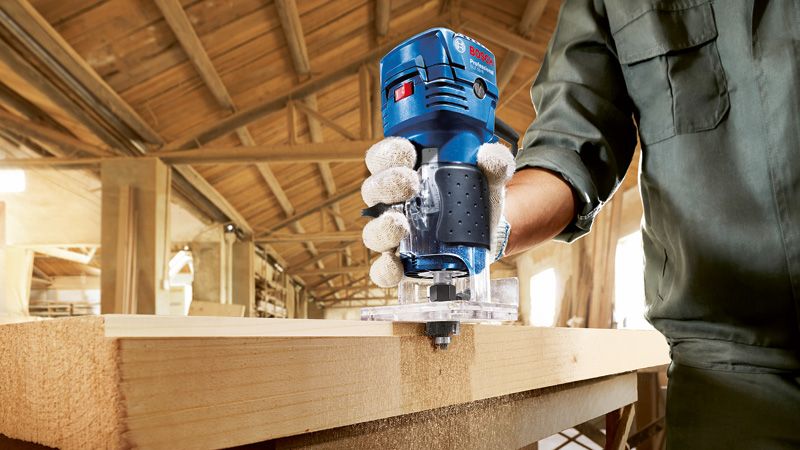 GLF 55-6 安全装備を身に着けた人が作業場でハンドヘルドルーターを使用して木材を加工しています。.