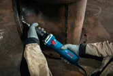 安全装備を身に着けた人が大きな金属パイプの溶接継ぎ目を研磨しています。