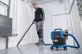 安全装置を装着した人がコードレス集塵機を使用してタイル張りの床を掃除しています。.