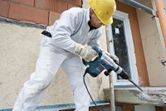 安全装備を身に着けた人が回転ハンマーを使用して建設現場でコンクリートを破壊しています。