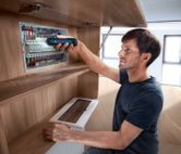 コードレスドライバーを使用して電気パネルのコンポーネントを固定する人。