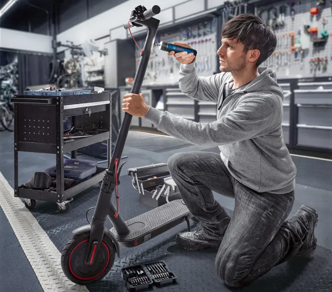 作業場でコードレスドライバーを使って電動スクーターを修理している人。.