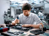 コードレスドライバーを使用して、作業台で電子部品を組み立てている人。