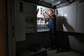 コードレス作業灯で照らされた電気パネルで作業する人。.