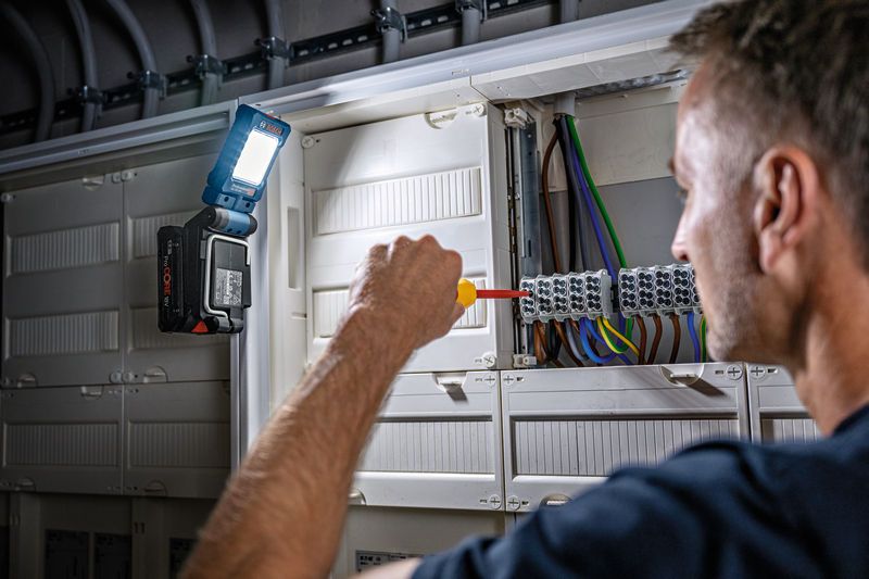 照明用にコードレスライトを取り付けた電気パネルでドライバーを使用する人。.