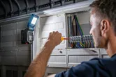 照明用にコードレスライトを取り付けた電気パネルでドライバーを使用する人。