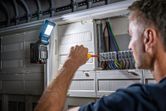 照明用にコードレスライトを取り付けた電気パネルでドライバーを使用する人。.
