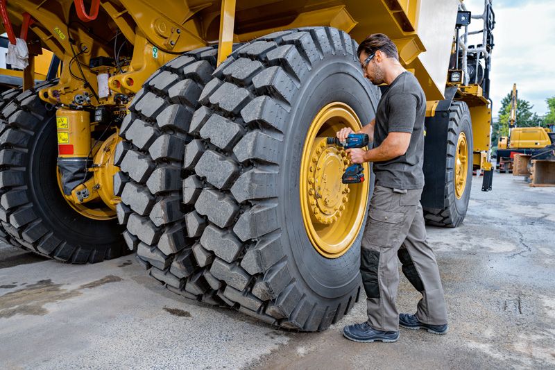安全装備を身に着けた人が、大型建設車両のタイヤにインパクトレンチを使用しています。.