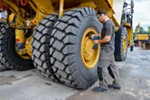 安全装備を身に着けた人が、大型建設車両のタイヤにインパクトレンチを使用しています。.