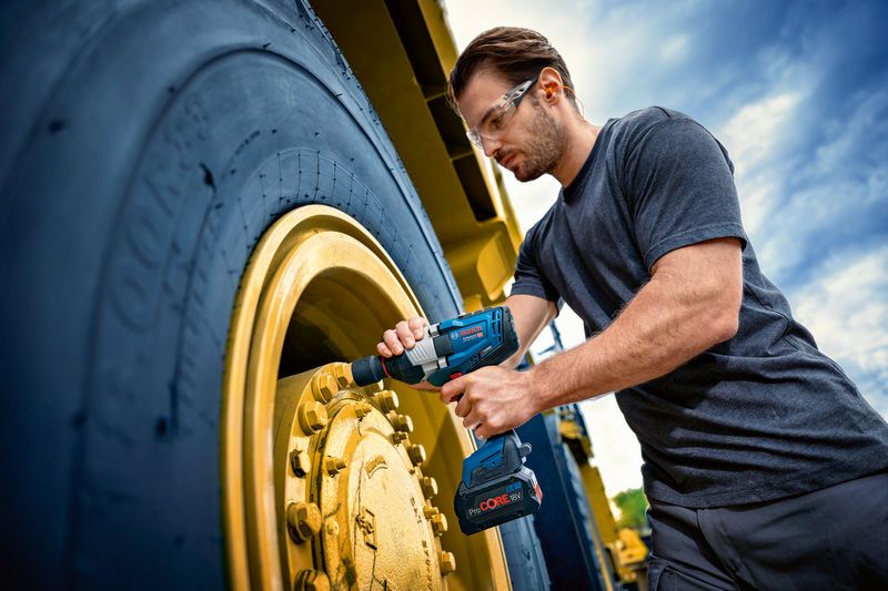 安全装備を身に着けた人が、車両の大型ホイールにインパクトレンチを使用しています。.