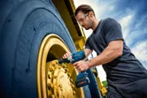 安全装備を身に着けた人が、車両の大型ホイールにインパクトレンチを使用しています。.
