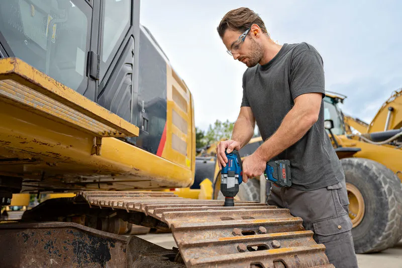 安全装置を装着した人が掘削機のトラック上でコードレスインパクトレンチを使用しています。.