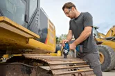 安全装置を装着した人が掘削機のトラック上でコードレスインパクトレンチを使用しています。.