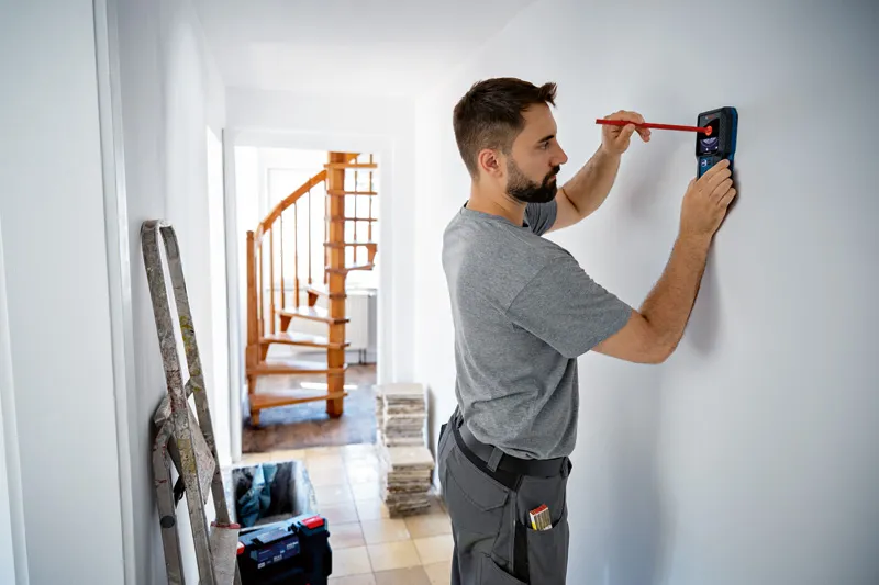 検出ツールを使用しながら鉛筆で壁に印を付けている人。.