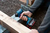 コードレスドリルを使用して木の梁にネジを締める人。.
