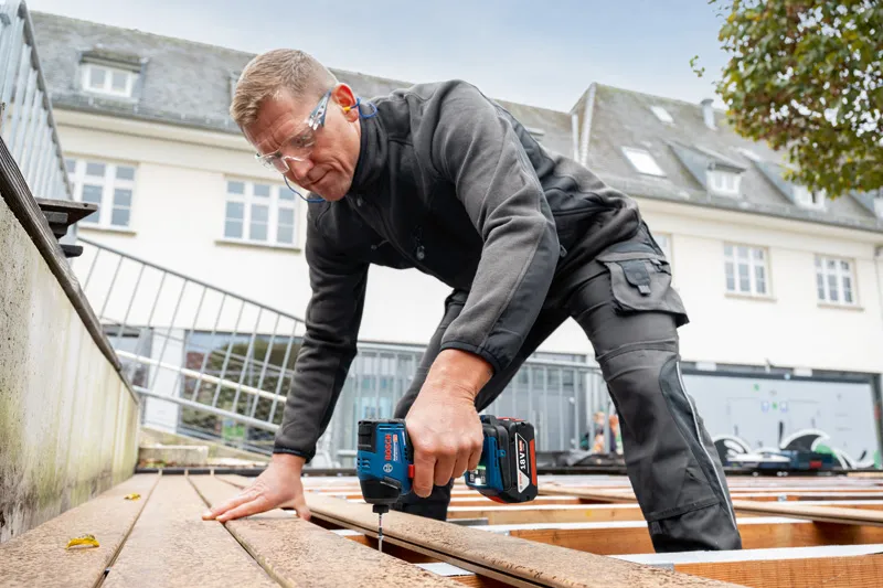 安全装置を装着した人がコードレスドリルを使用してデッキ板を固定しています。.