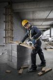 安全装備を身に着けた人がコンクリートブロックの上で丸鋸を使って木材を切っています。