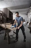 安全装備を身に着けた人が作業場でコードレス丸鋸を使って木材を切っています。